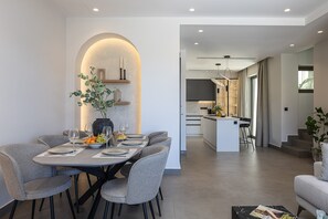 A modern dining area with a round table, grey chairs, and a vase with greenery. - Maple Villa 2 Superior Sea View Villa, Walking Distance From Plakias Beach (Agios Vasileios)