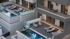 Ein mehrstöckiges, modernes Gebäude mit Glasbalkonen, Außenbereichen zum Sitzen und einem Pool auf dem Dach.