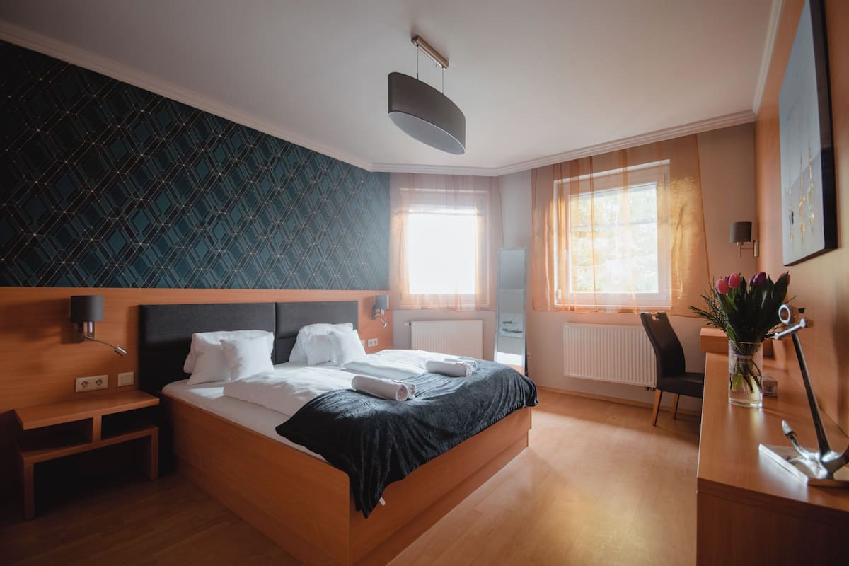 Ett modernt hotellrum med en stor säng, ett skrivbord, en stol, en skrivbordslampa och ett fönster med gardiner.