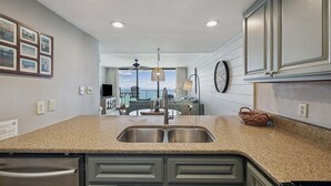 A kitchen with a granite countertop, stainless steel sink, and dark cabinetry. - Seagrove Sunrise 1004-Beachfront Views-Sleeps 6 (Seagrove Beach)