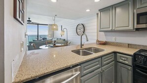A kitchen with granite countertops, stainless steel appliances, and a dining area with a view. - Seagrove Sunrise 1004-Beachfront Views-Sleeps 6 (Seagrove Beach)
