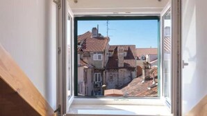 Una finestra con vista su un paesaggio urbano, che include edifici con tetti in tegole rosse e un cielo azzurro intenso.