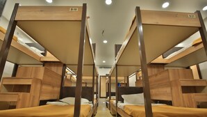Unas literas dispuestas en fila, con estructura de madera y ropa de cama color beige, identificadas como B-19 y B-20.