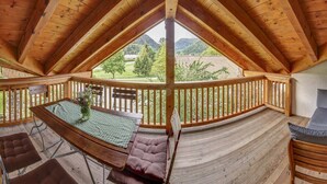 En træterrasse med et bord og stole, en polstret bænk og udsigt over et grønt landskab.