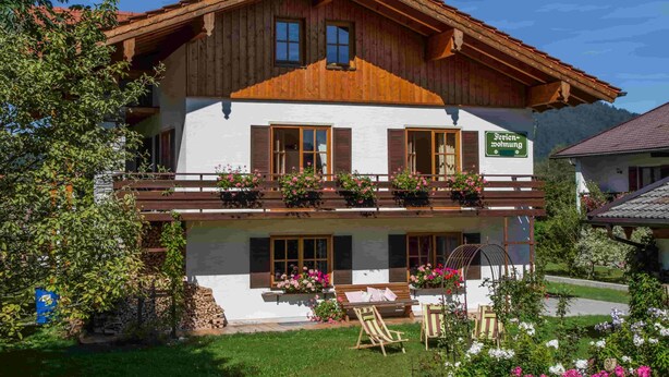 A two-story wooden building with a balcony, a sign indicating it is a guesthouse, and a garden with flowers and seating. - "Zeitlos" Vacation Rental for 6 Adults and 1 Child, 3 Bedrooms, 100 m² (Inzell)
