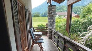 A balcony with wooden chairs and tables, a stone pillar, and a view of a green landscape with mountains. - "Zeitlos" Vacation Rental for 6 Adults and 1 Child, 3 Bedrooms, 100 m² (Inzell)