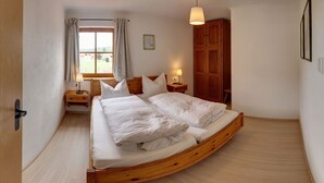 A bedroom with a curved wooden bed, a window with curtains, a bedside lamp, and a wooden wardrobe. - "Zeitlos" Vacation Rental for 6 Adults and 1 Child, 3 Bedrooms, 100 m² (Inzell)