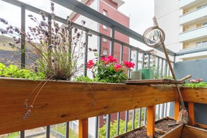 A balcony with a wooden railing, a hanging bird feeder, and potted plants including flowers and greenery. - Serene 2BDR Retreat by Holyrood Park (Edinburgh)