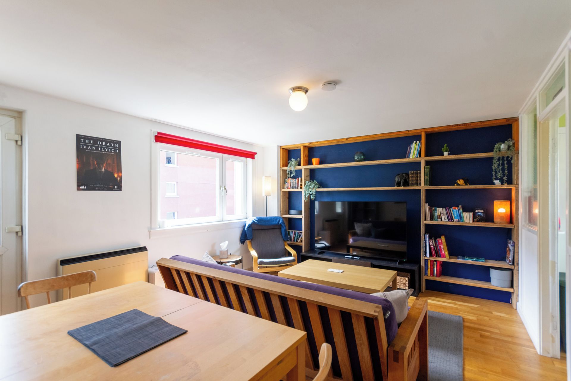 A cozy living room with a wooden dining table, a comfortable sofa, a bookshelf, and a television.