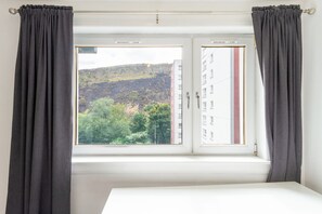 A room with a window, curtains, and a view of a hillside. - Serene 2BDR Retreat by Holyrood Park (Edinburgh)