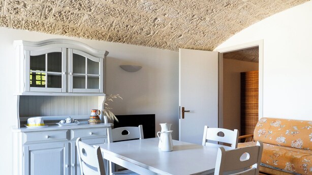Ein weißer Esstisch mit Stühlen, eine weiße Schranke mit Glastüren und ein Sofa mit floralem Bezug.