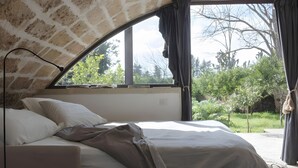 A bedroom with a bed, a window, and a view of greenery.