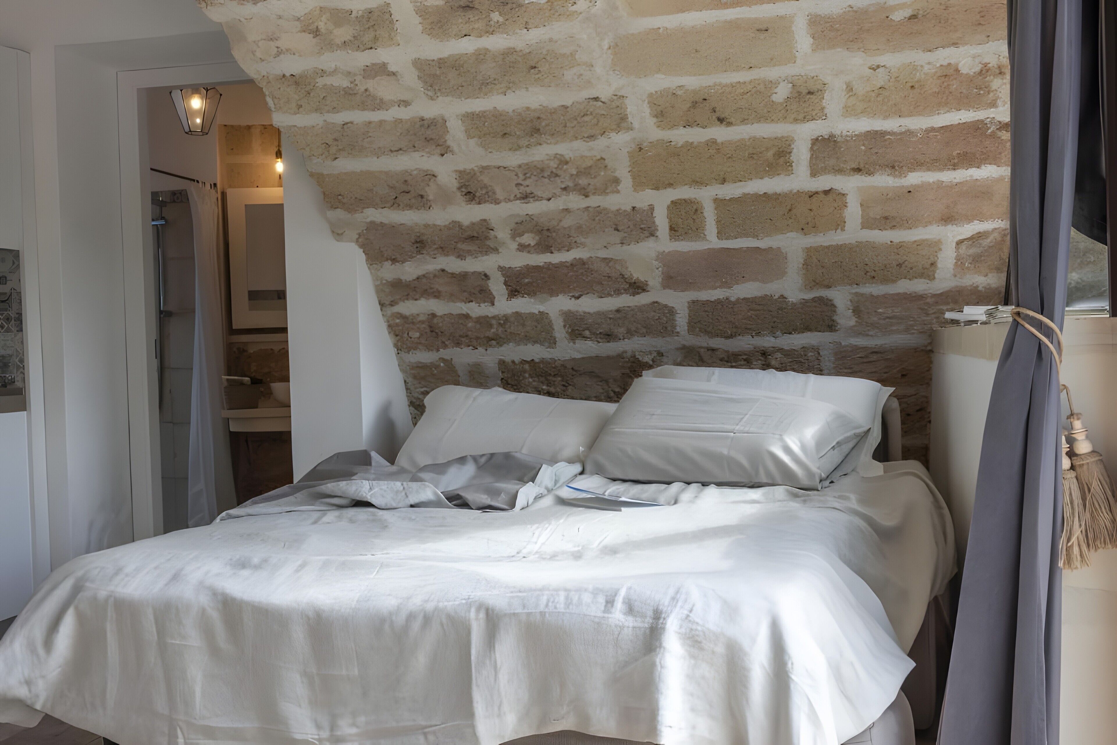 A bedroom with a brick wall, a bed with white bedding, a bedside table, and a hanging light fixture.
