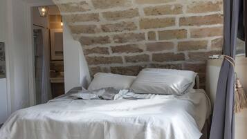 A bedroom with a brick wall, a bed with white bedding, a bedside table, and a hanging light fixture.