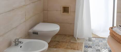 A bathroom with a bidet, toilet, and a shower area.