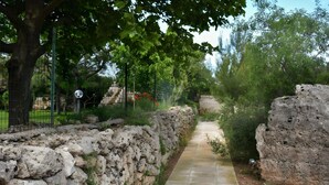 A stone pathway flanked by a stone wall and trees, leading to a fenced area.