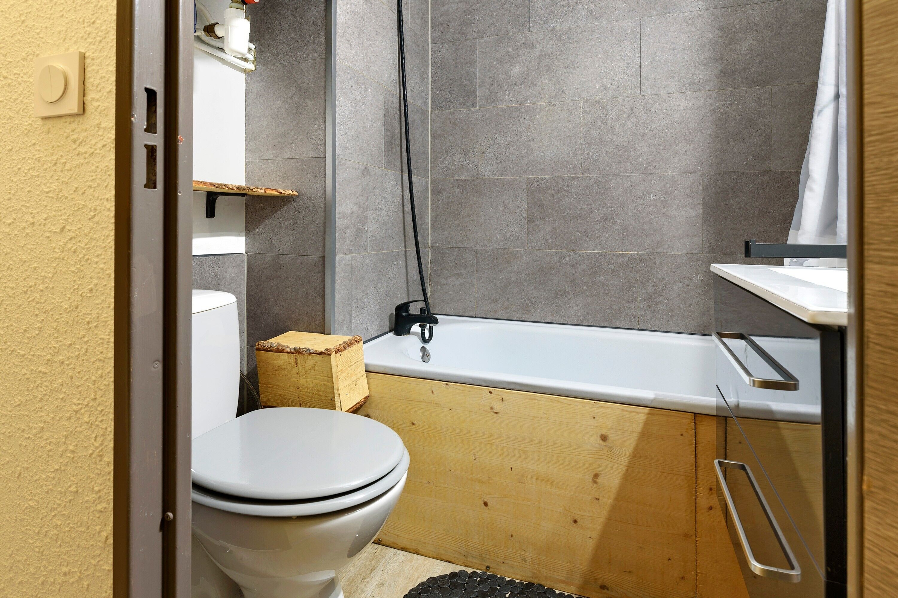 A bathroom with a toilet, a wooden cabinet, a bathtub, and a shower curtain.