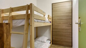 Une chambre avec un lit superposé, une porte en bois et un petit placard.