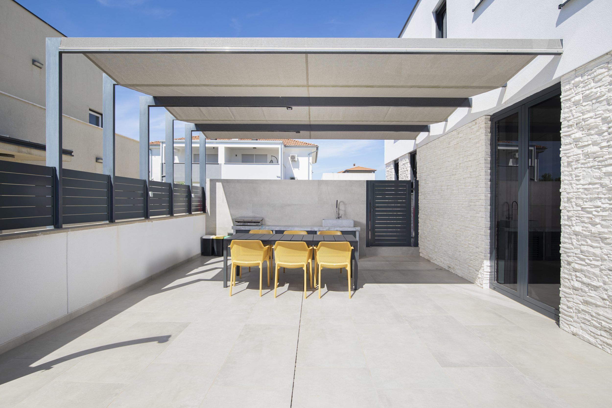 Un patio techado al aire libre con una mesa, sillas, una parrilla y un muro de piedra.