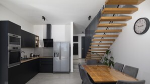 Eine moderne Küche mit integrierten Geräten, ein Essbereich mit einem Holztisch und Stühlen sowie eine Treppe mit Holzstufen.