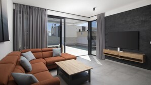 Ein modernes Wohnzimmer mit einer Eckcouch, einem Couchtisch, einem Fernseher und einer Schiebetür zu einer Terrasse.