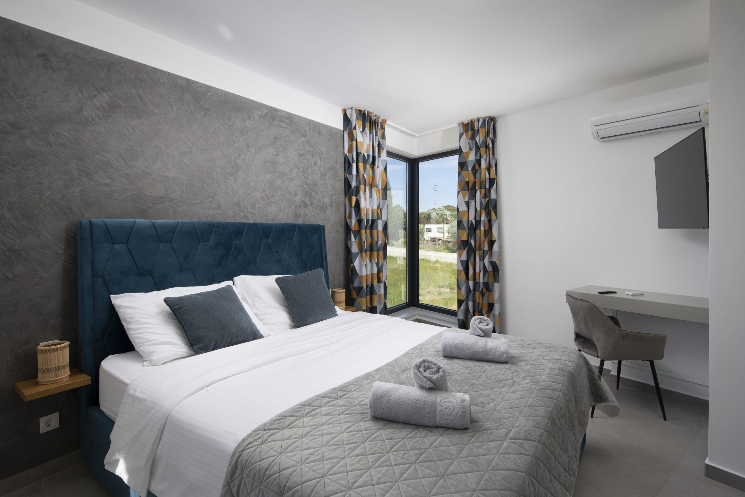 A modern hotel room with a large bed, a desk, and a window with curtains.