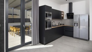 Eine moderne Küche mit Einbauofen, Mikrowelle und Kühlschrank, ein Essbereich mit gelben Stühlen und eine Glastür, die zu einem Außenbereich führt.