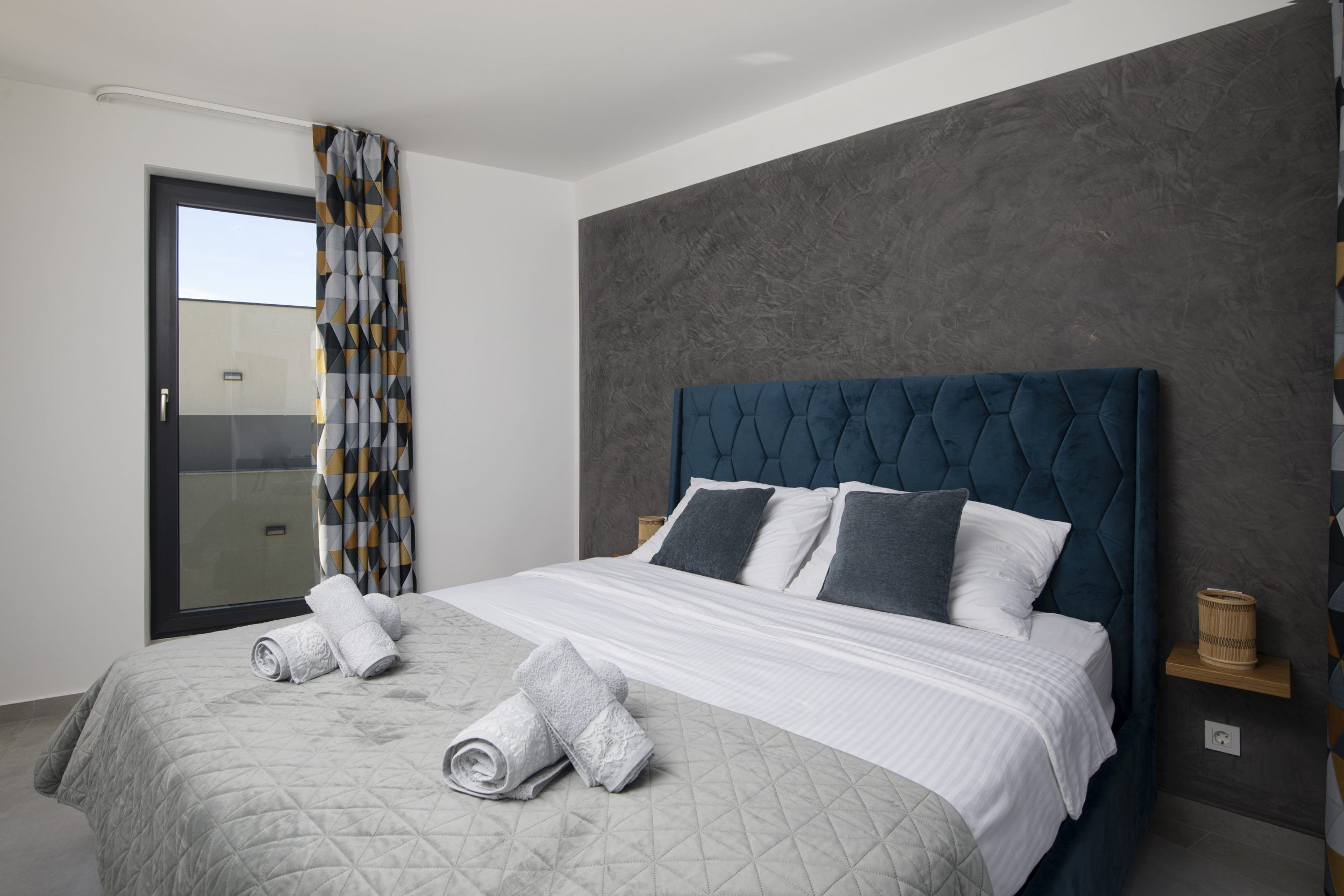 A modern bedroom with a large bed, a sliding glass door, and a textured wall.