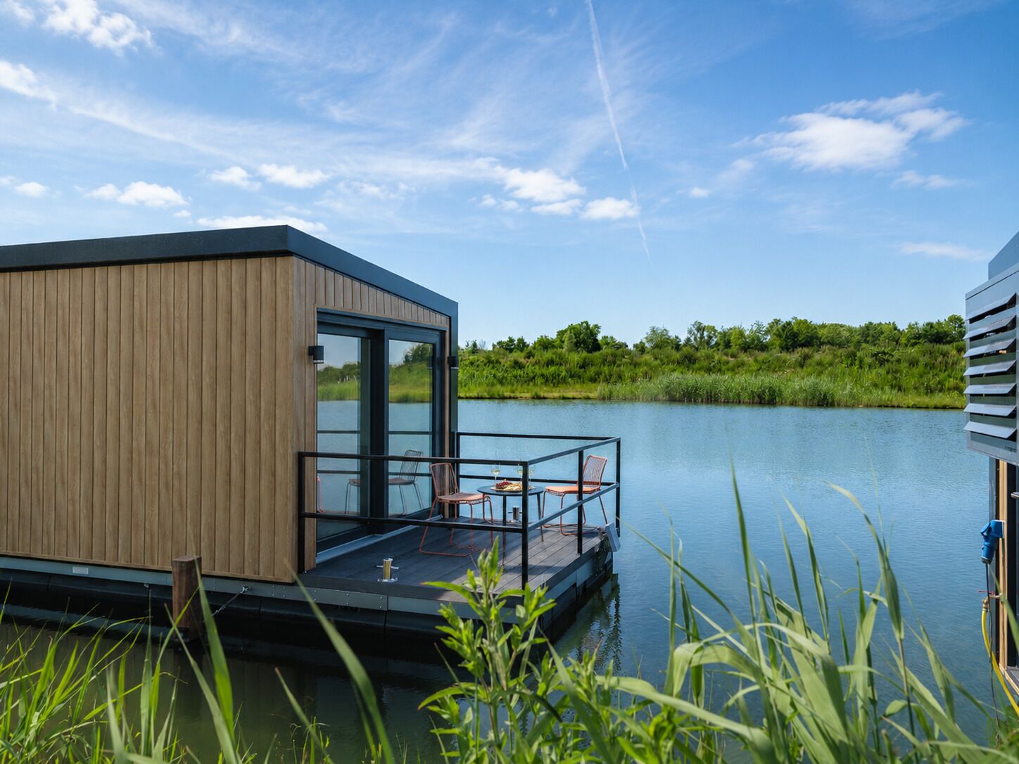Eine moderne, schwimmende Struktur mit Holzfassade, Glasüren und einem Deck mit Stühlen und einem Tisch.