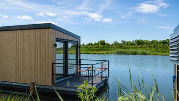 Eine moderne, schwimmende Struktur mit Holzfassade, Glasüren und einem Deck mit Stühlen und einem Tisch.