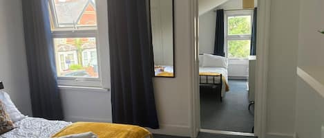 A hotel room with a bed, a mirror, a window with curtains, and a view of the street.