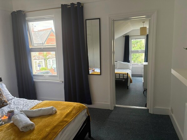Habitación de hotel con cama, espejo, ventana con cortinas y vista a la calle.