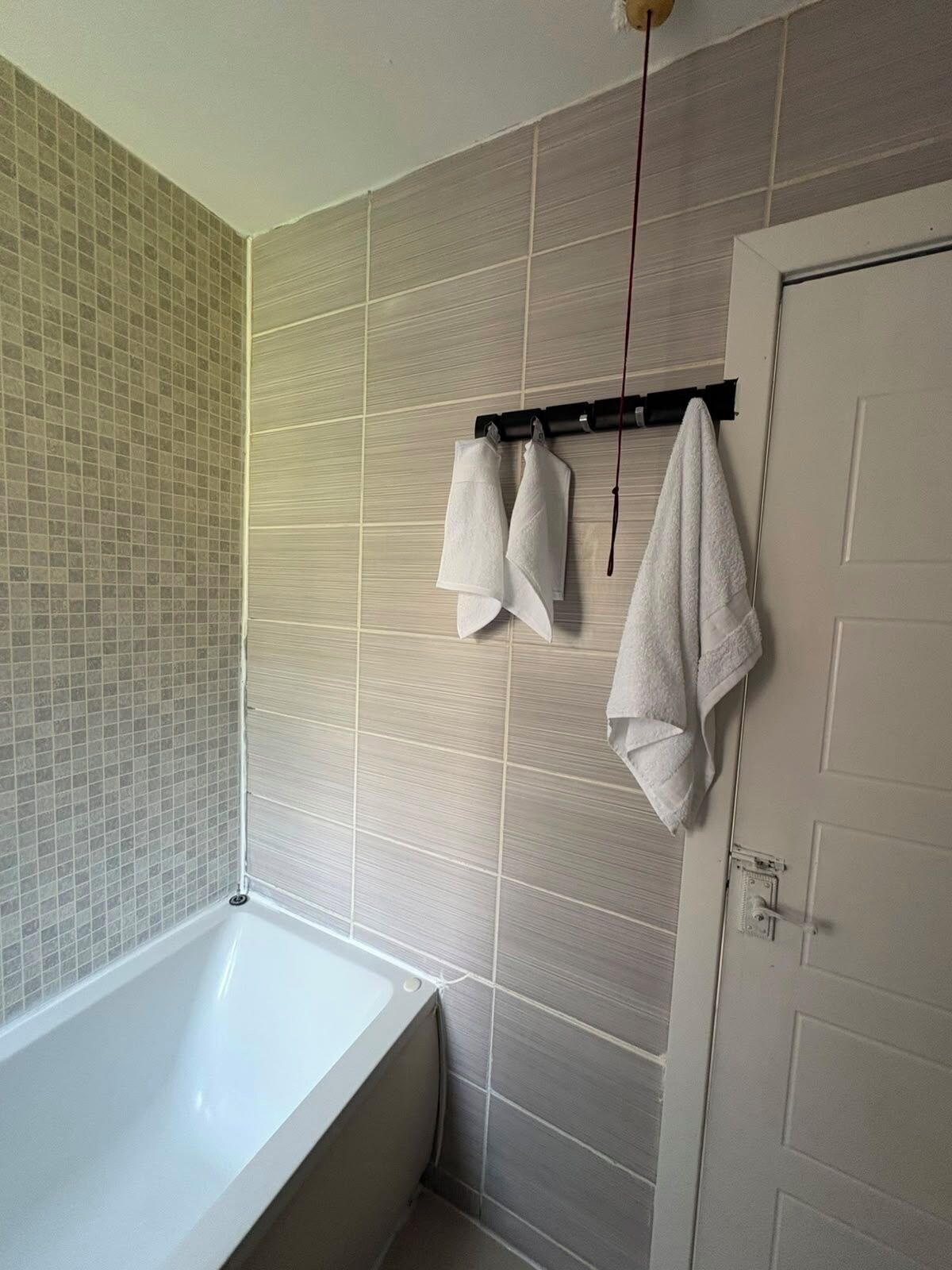 A bathroom with a bathtub, tiled walls, and a towel rack with towels.