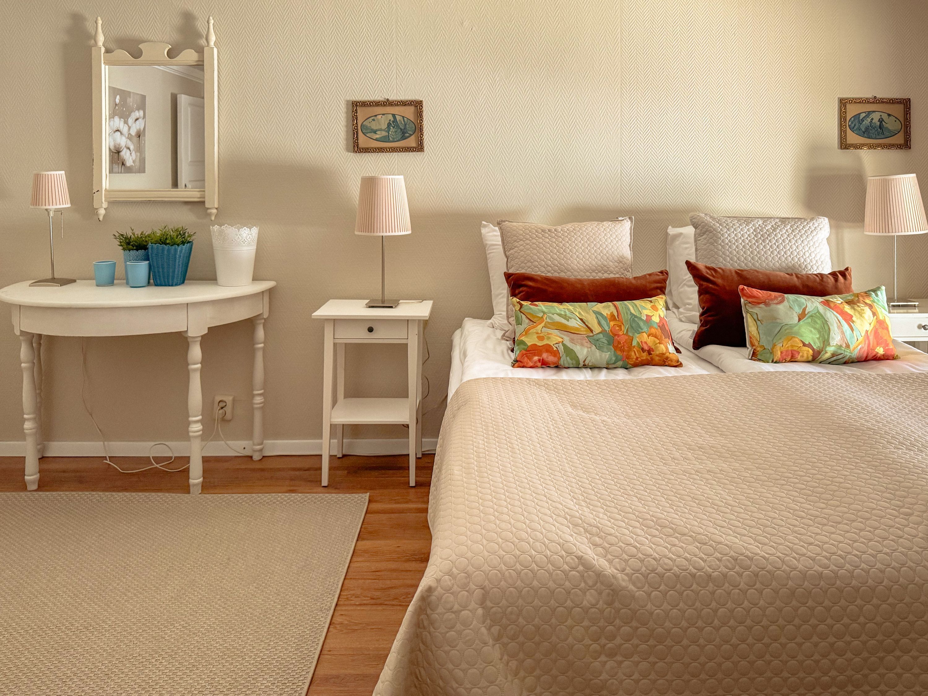 Un dormitorio con cama, mesitas de noche, lámparas, un espejo y almohadas decorativas.