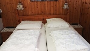 Una cama doble con ropa blanca en una habitación de madera con dos mesitas de noche y lámparas de pared.