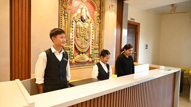 A reception desk with a decorative wall behind it, a wooden paneling design, and a ceiling fan. - HOTEL SIYAGRAND (Tirupati)
