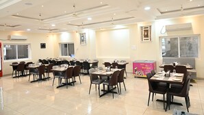 A spacious dining area with multiple tables and chairs, ceiling fans, and an air conditioning unit. - HOTEL SIYAGRAND (Tirupati)