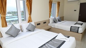 A hotel room with two beds, a window with curtains, an air conditioning unit, and a view of the city. - HOTEL SIYAGRAND (Tirupati)