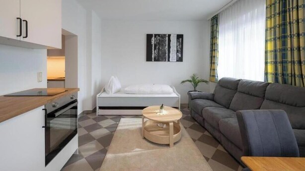 Un espacio habitable compacto con kitchenette, un sofá, una mesita redonda y una cama.