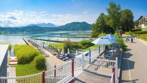 Terraza junto al lago con sillones, una mesita y una sombrilla azul.