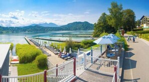 A lakeside deck with lounge chairs, a small table, and a blue umbrella. - C14 - Seewirt Apartments: 1-Bedroom Apartment with Shower (St. Kanzian am Klopeiner See)