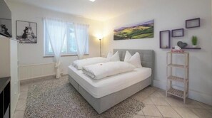 A bedroom with a bed, a window with curtains, a bedside lamp, a wall-mounted shelf, and a painting. - C14 - Seewirt Apartments: 1-Bedroom Apartment with Shower (St. Kanzian am Klopeiner See)