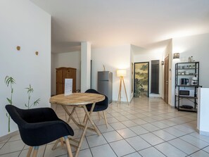 Un coin repas comprenant une table ronde, deux chaises, une lampe, un réfrigérateur et une étagère contenant des ustensiles de cuisine.