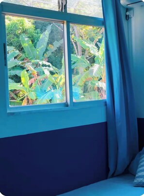 Ein Zimmer mit Fensterblick auf einen Garten, einem Bett und einem Vorhang.