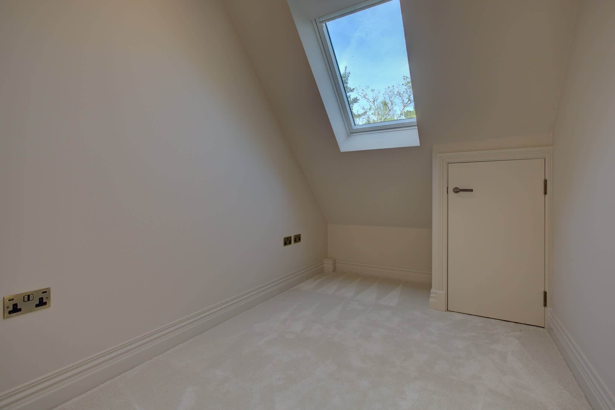 A room with a sloped ceiling, a skylight, a door, and a power outlet.