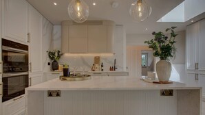 Een moderne keuken met witte kasten, een centraal eiland, hanglampen en uitzicht naar buiten.