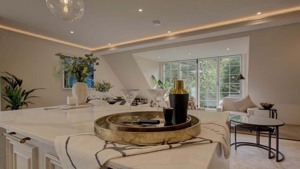 Een moderne keuken met een marmeren aanrecht, een zithoek met een witte bank, en een groot raam dat natuurlijk licht binnenlaat.