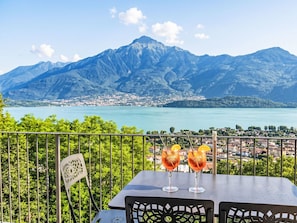 Ein Tisch mit zwei Aperol Spritz Cocktails, einem Metallstuhl und einem malerischen Blick auf Berge und einen See.