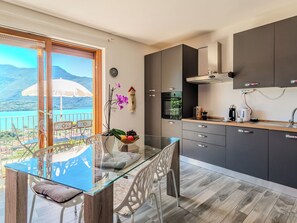 Eine moderne Küche mit einem Glastisch, grauen Schränken und Blick auf einen Bergsee.