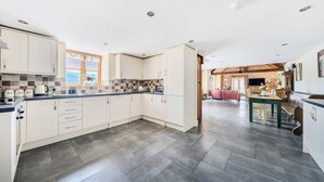 A spacious kitchen with white cabinets, a tiled backsplash, and a view to the living area. - The Dairy (Corwen)